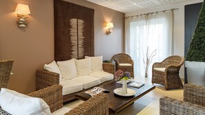 A modern living room with a sofa, two wicker chairs, a coffee table with a vase and magazine, and a wall-mounted lamp.
