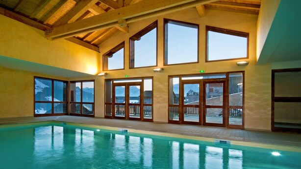 An indoor swimming pool with large windows and wooden beams. - Appartement à Hauteluce, navette gratuite (Hauteluce)