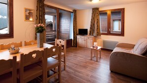 A cozy living room with a wooden dining table, chairs, a sofa, and a TV. - Appartement à Hauteluce, navette gratuite (Hauteluce)