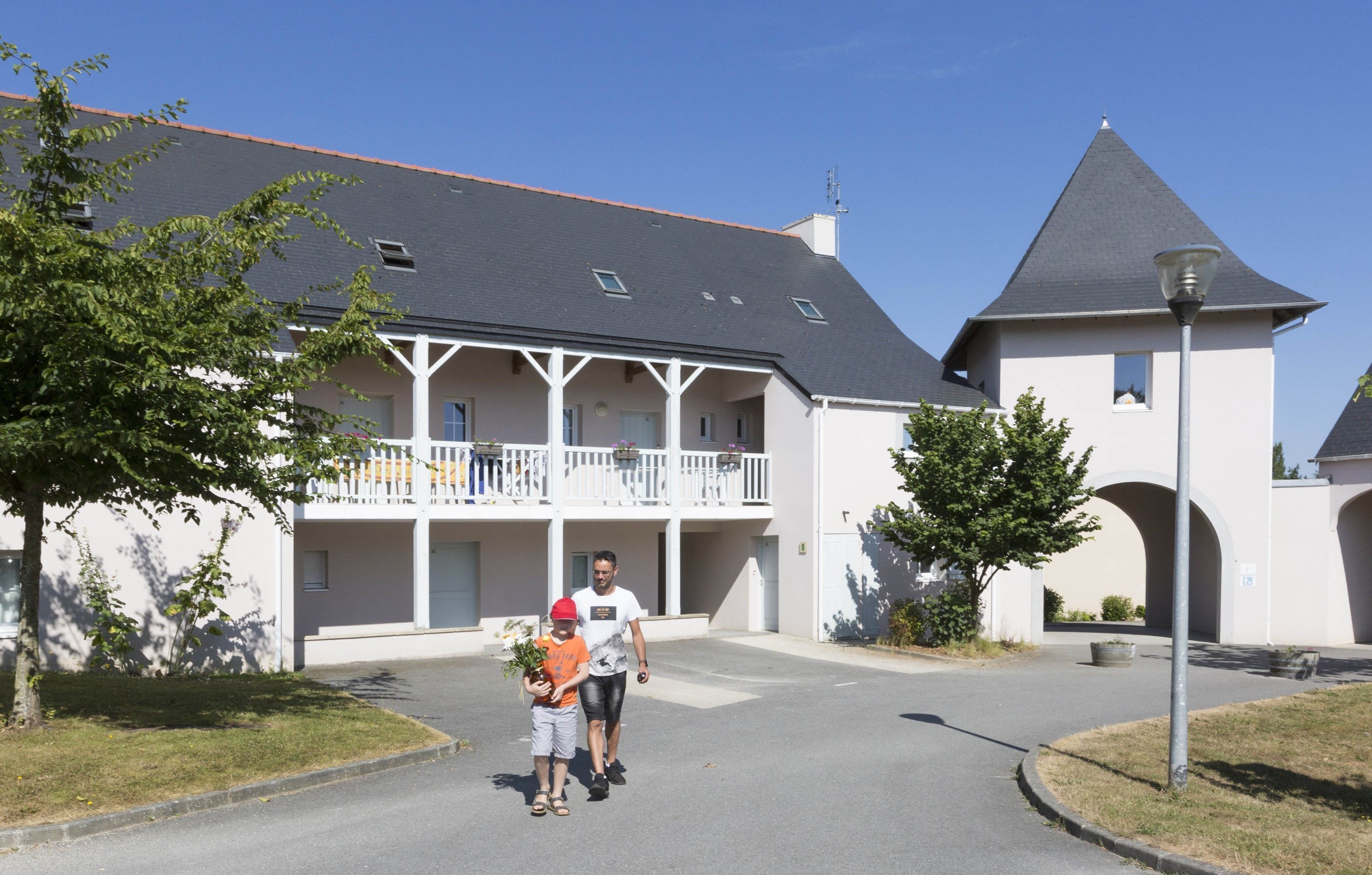A two-story building with a balcony, a tower-like structure, and a paved driveway.