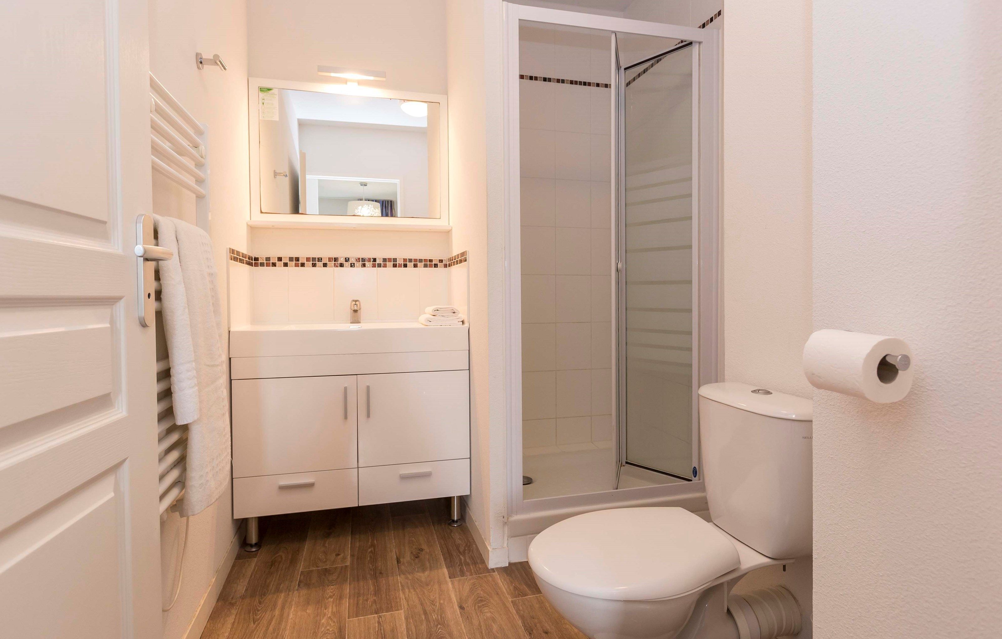 A bathroom with a toilet, sink, mirror, and shower.