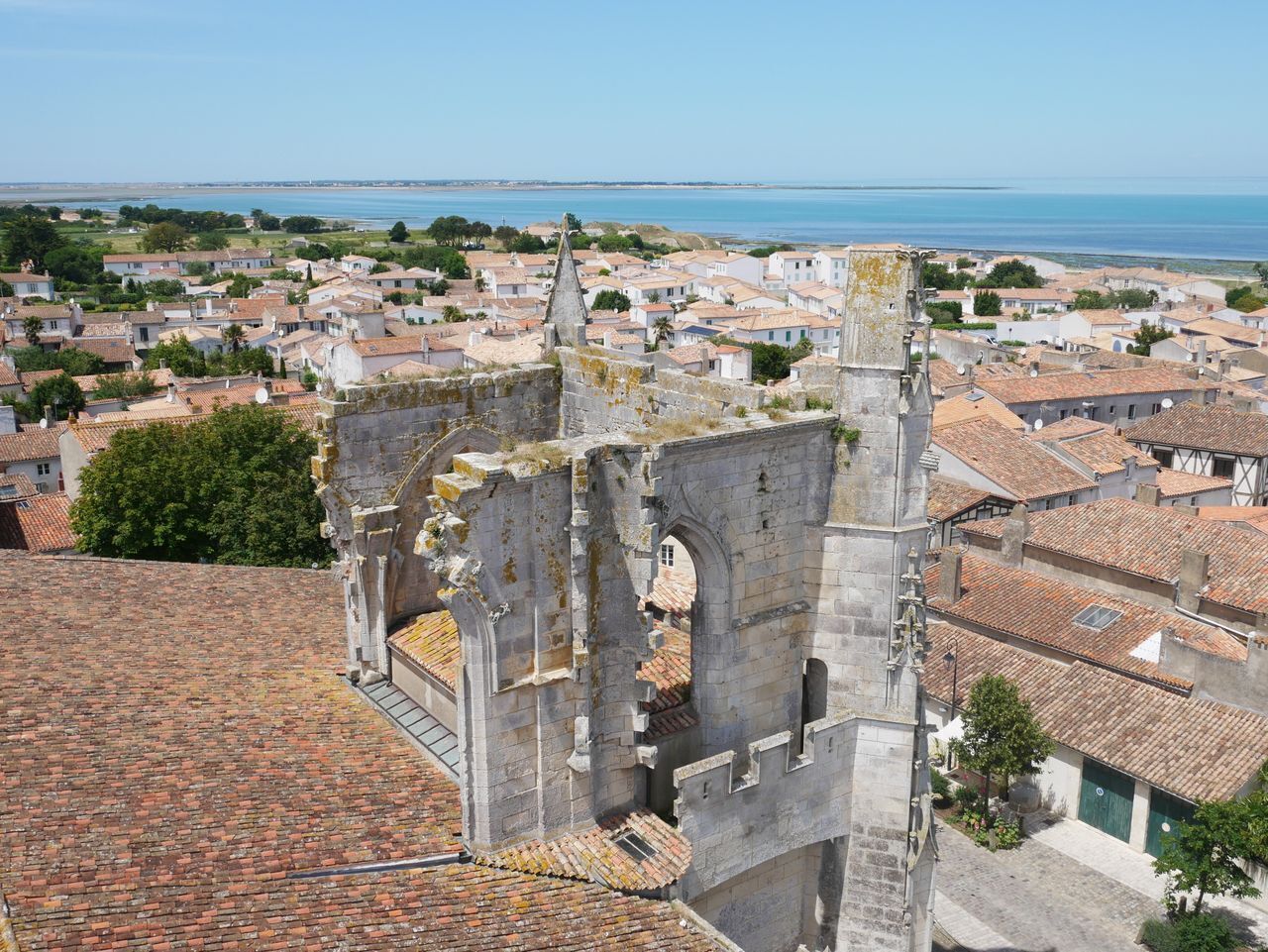 Une tour de pierre historique, dotée d’ouvertures en arc, entourée de bâtiments traditionnels aux toits recouverts de tuiles rouges.