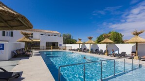 Una piscina con sillas de descanso y sombrillas, rodeada de edificios con paredes blancas y tejados de azulejos.