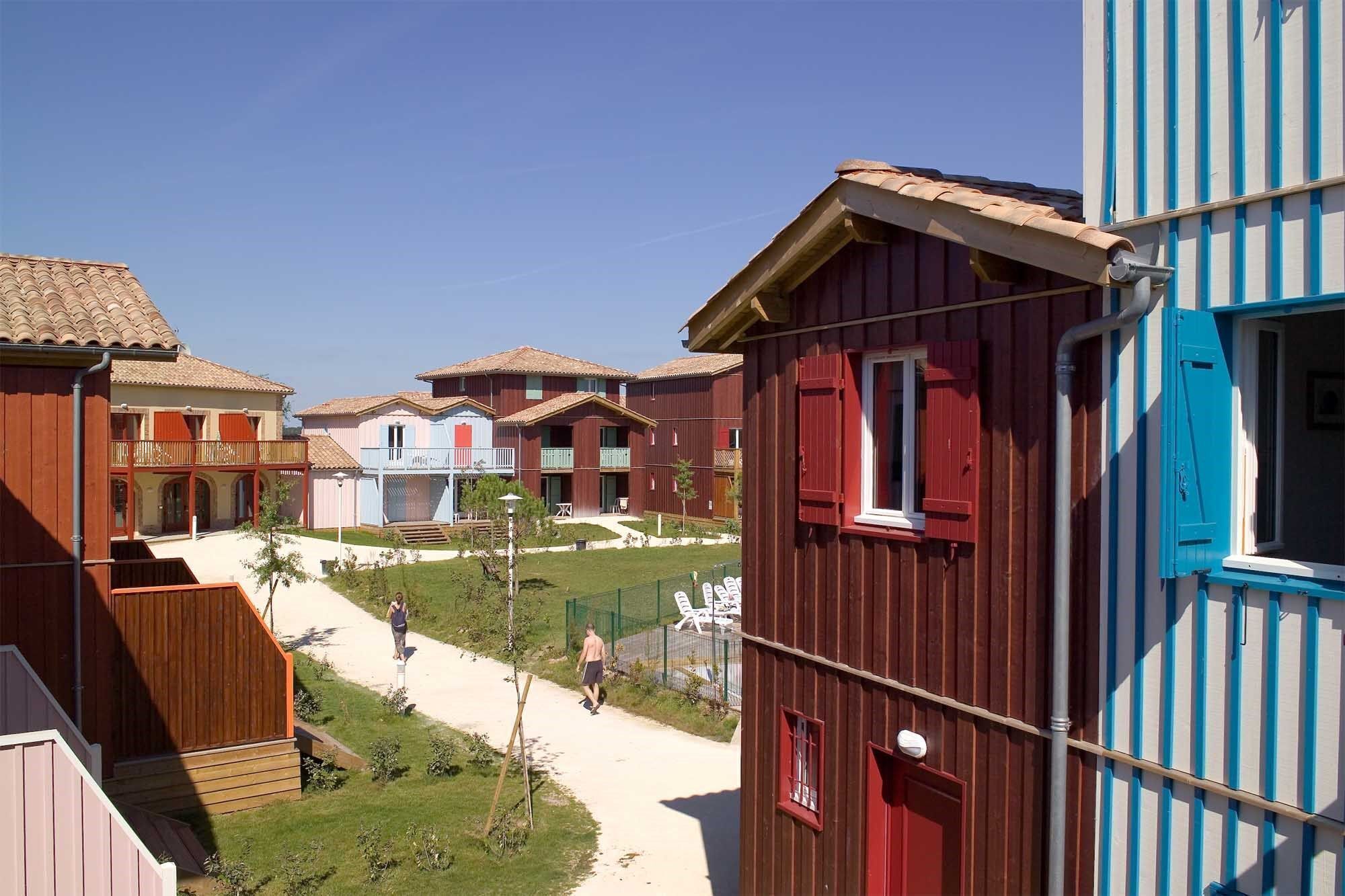 A row of wooden buildings with balconies, a paved walkway, and a clear sky.