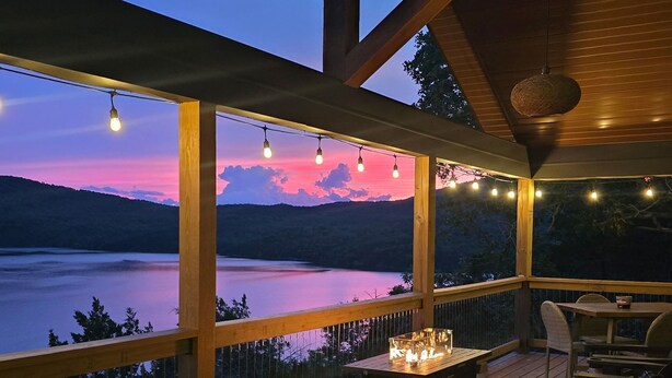 Une terrasse en bois avec des sièges extérieurs et une vue sur un lac au crépuscule.