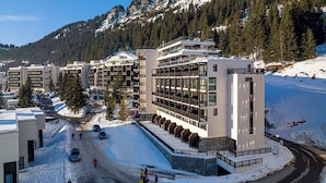 Un hotel modern amb diverses plantes, una pista d'esquí al fons i un paisatge cobert de neu.