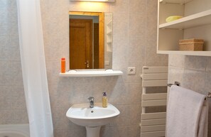 Une salle de bain avec un lavabo blanc, un miroir, un porte-serviettes et une étagère contenant des articles de toilette.