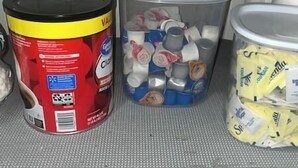 Three containers on a shelf: a red canister labeled 'VAL', a clear plastic bin with metal lids, and a yellow bag with 'Dukka' branding. - Historic Craftsmen Style Home (Shreveport)