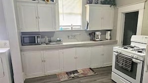 A kitchen with white cabinets, a microwave, a stove, and a sink. - Historic Craftsmen Style Home (Shreveport)