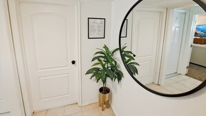 Ein Flur mit weißen Türen, einem Blumentopf, einem gerahmten Zertifikat und einem runden Spiegel an der Wand.
