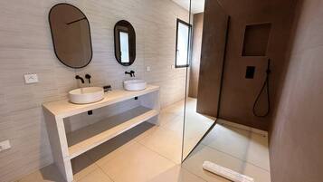 A modern bathroom with two sinks, a large mirror, and a shower area.