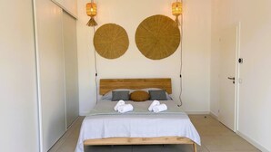 A neatly made bed with a wooden headboard, two wall-mounted lamps, and two large woven wall decorations.