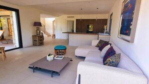 A modern living room with a white sofa, a coffee table, and a dining area with a kitchen in the background.