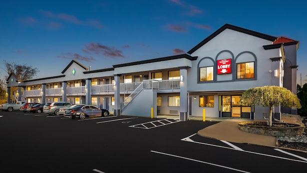 Een motel met een gebouw van twee verdiepingen, een zichtbare trap en een parkeerplaats met meerdere auto's.