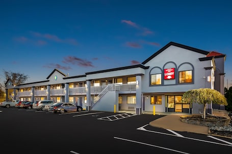 A motel with a two-story structure, a visible staircase, and a parking lot with several cars.