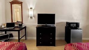 Een hotelkamer met een bureau, een televisie, een magnetron en een bed met rode beddengoed.