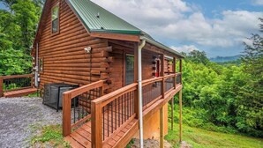 Eine Blockhütte mit grüner Dachdeckung, einem Balkon und einer Schotterauffahrt.