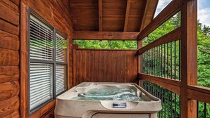 Eine Holzterrasse mit Whirlpool, Holzgeländern und Blick ins Grüne.