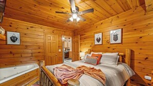 Ein Schlafzimmer in einer Holzhütte mit einem Bett, einem Deckenventilator und einem Badezimmer mit einer Badewanne.