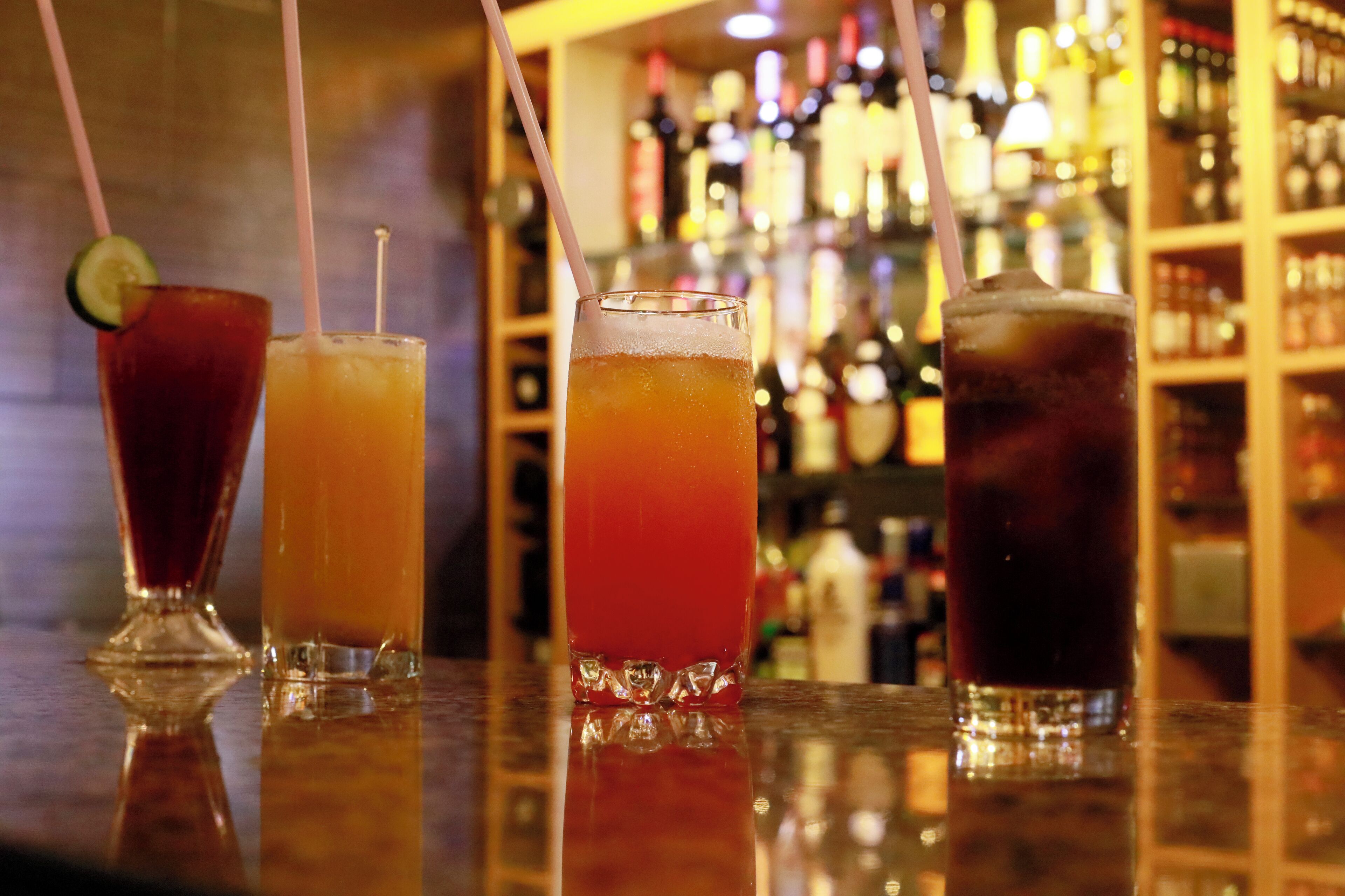 A bar with four glasses of various beverages, each with a straw.