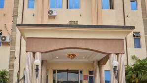 L’entrée d’un hôtel, avec une grande porte en verre, un lustre central et deux lampadaires de chaque côté.