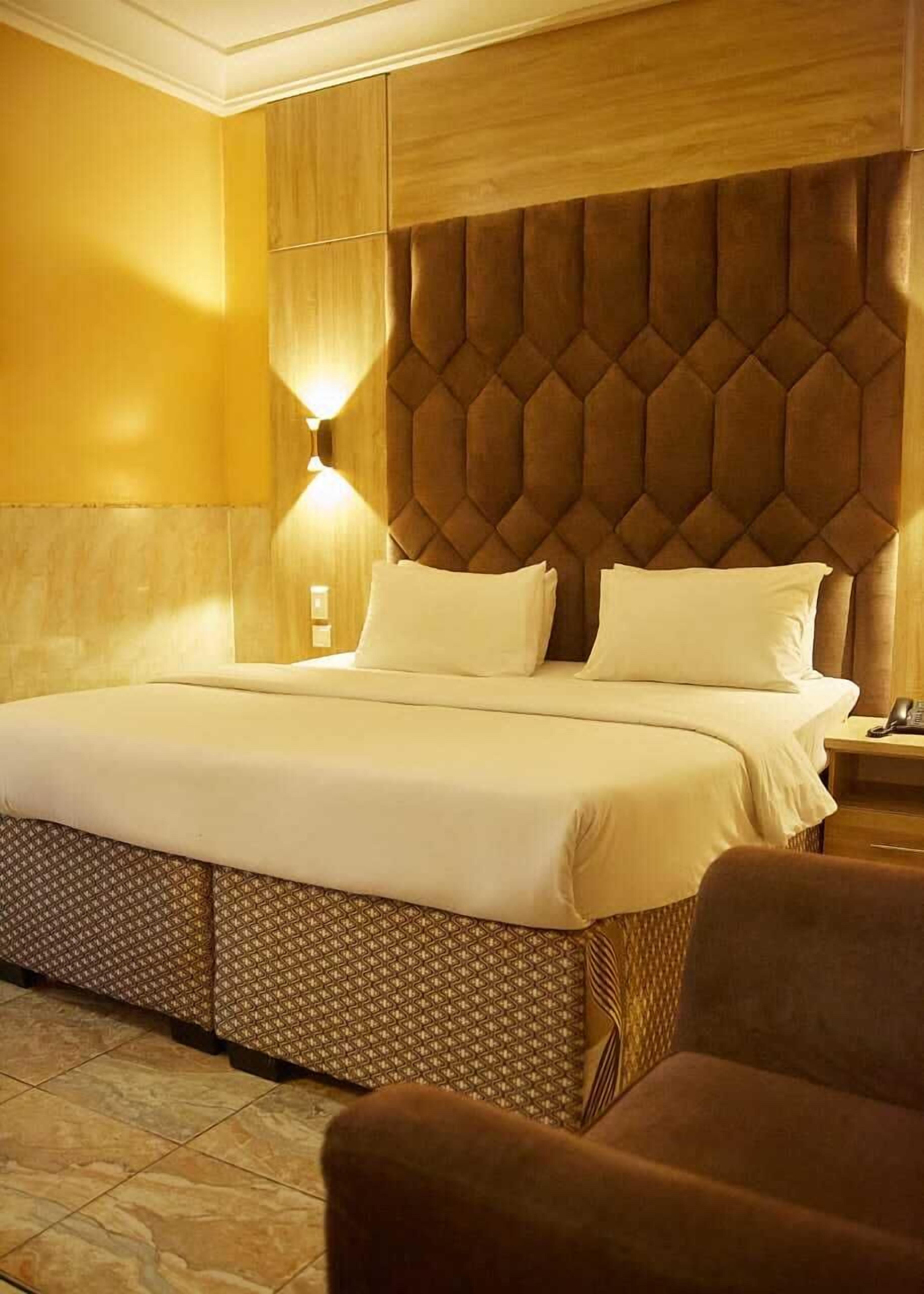 A hotel room with a large bed, a wooden headboard, and a bedside table with a phone.