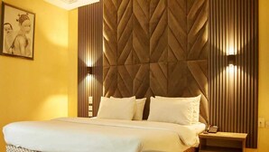 Une chambre d’hôtel avec un grand lit, une table de chevet avec un téléphone et un luminaire fixé au mur.