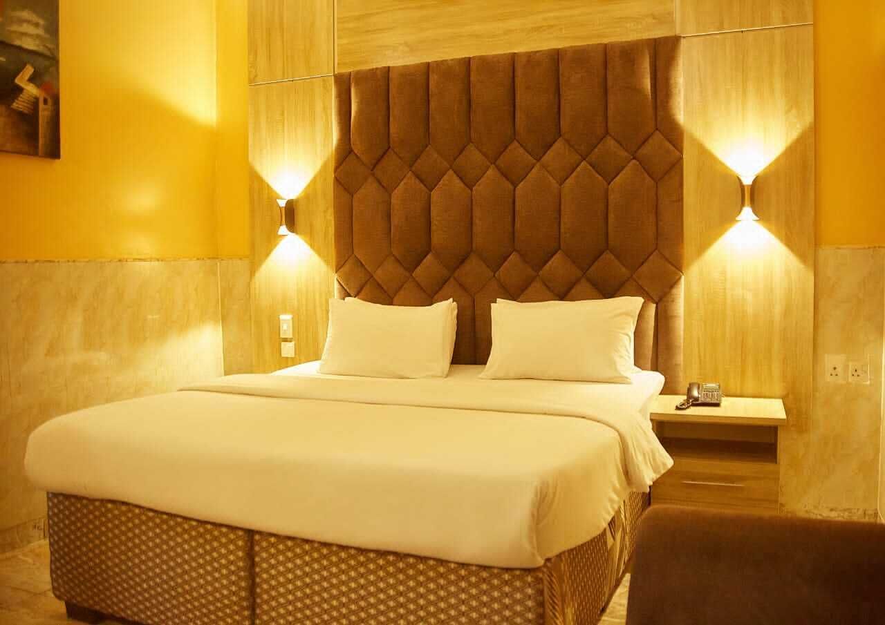 Una cama grande con cabecera acolchada, dos lámparas de noche y una mesita con un teléfono.