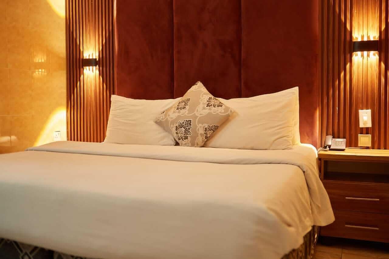 A hotel room with a large bed, a wooden headboard, and a nightstand with a phone and lamp.
