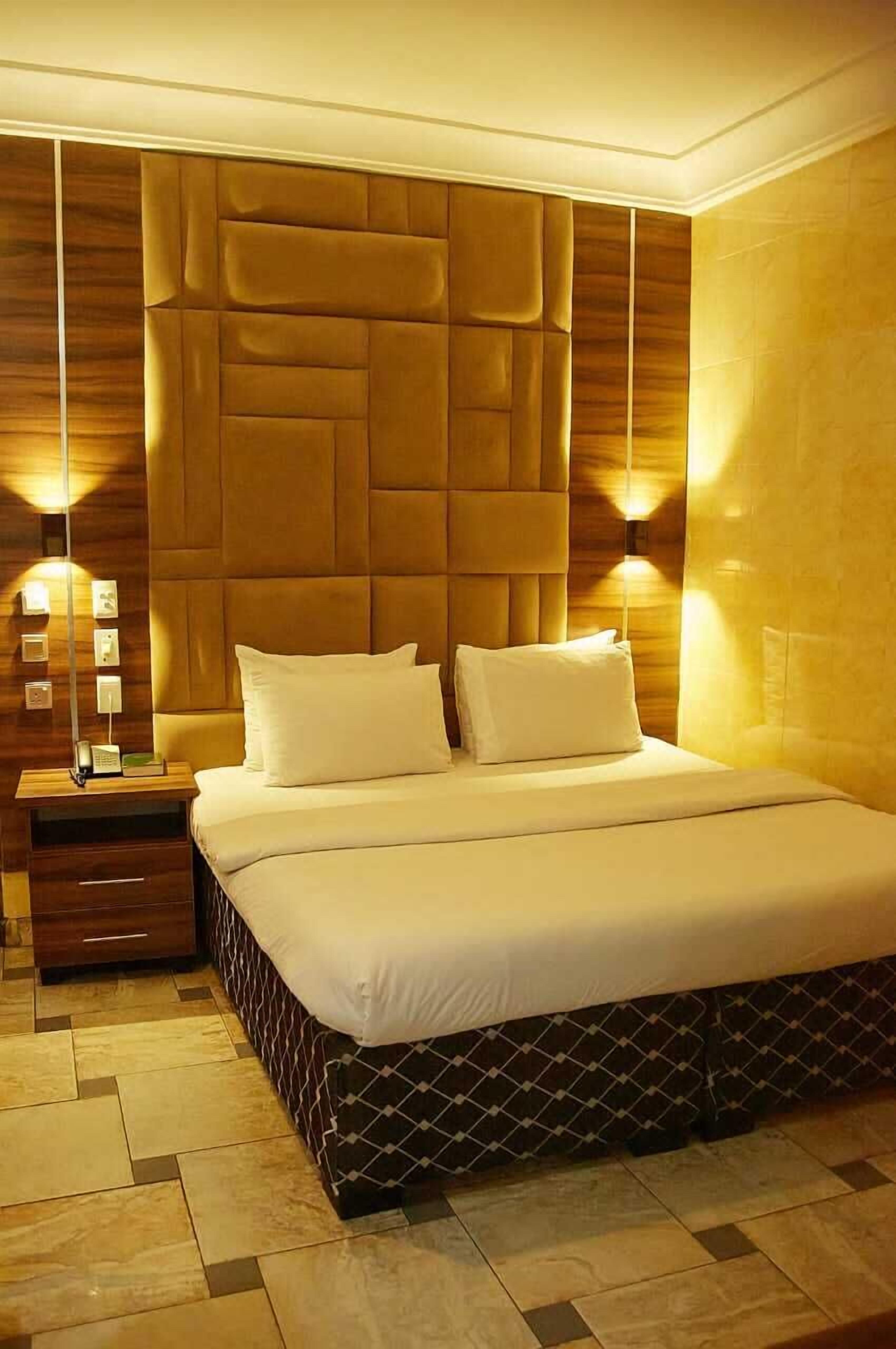 Un dormitorio moderno con cabecera capitonada, una cama bien hecha y una mesita de noche con lámpara.