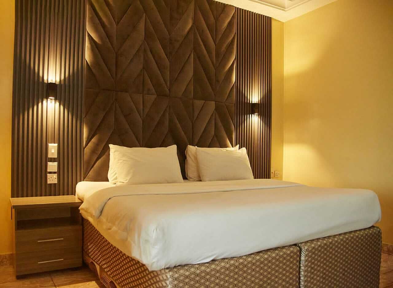 A hotel room with a large bed, a wooden headboard, and a nightstand with drawers.
