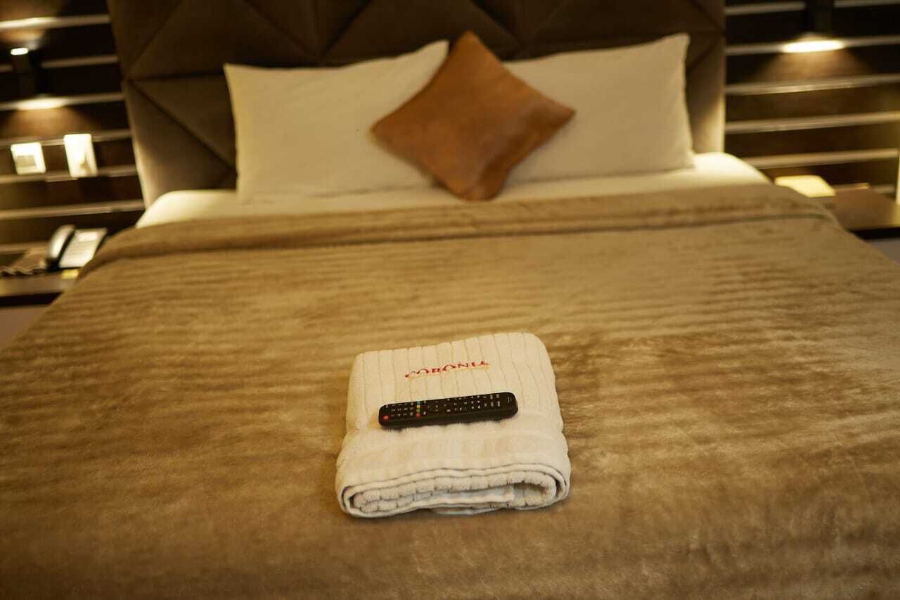 Een opgemaakt bed met een gevouwen handdoek en een afstandsbediening erop.