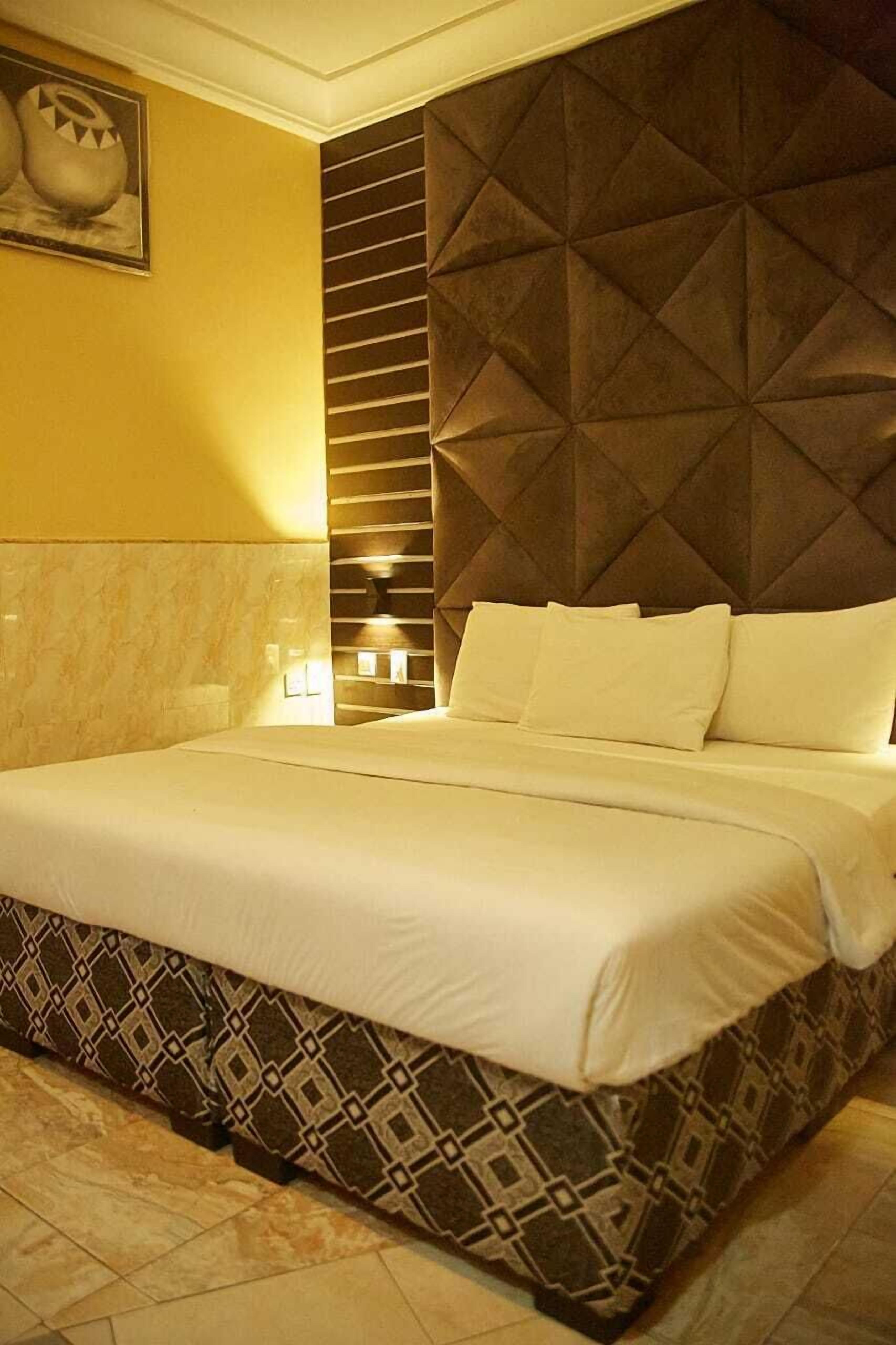 Ein Hotelzimmer mit einem großen Bett, einem gemusterten Bettvorhang, einem geometrischen Kopfteil und einer Wandleuchte.