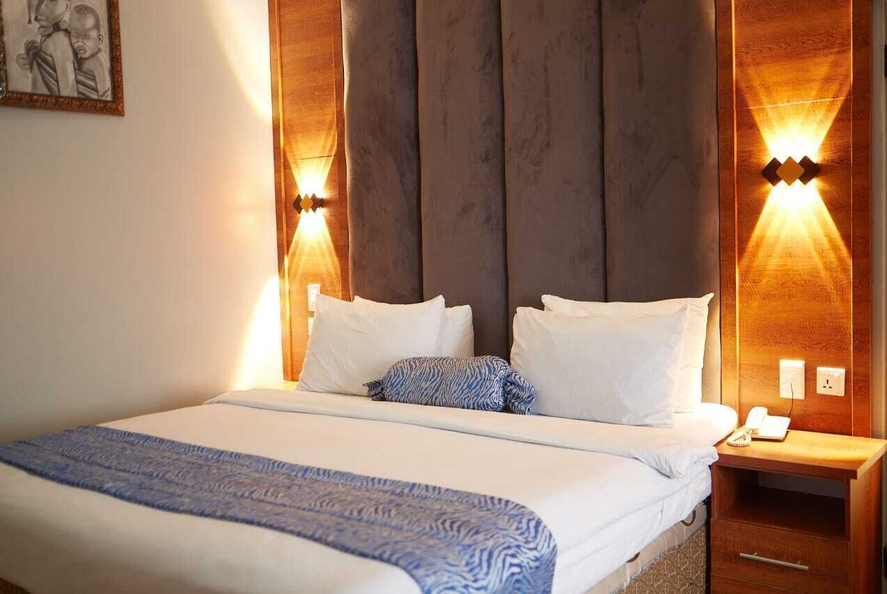 Una habitación de hotel con una cama grande, dos mesitas de noche y una lámpara fijada en la pared.