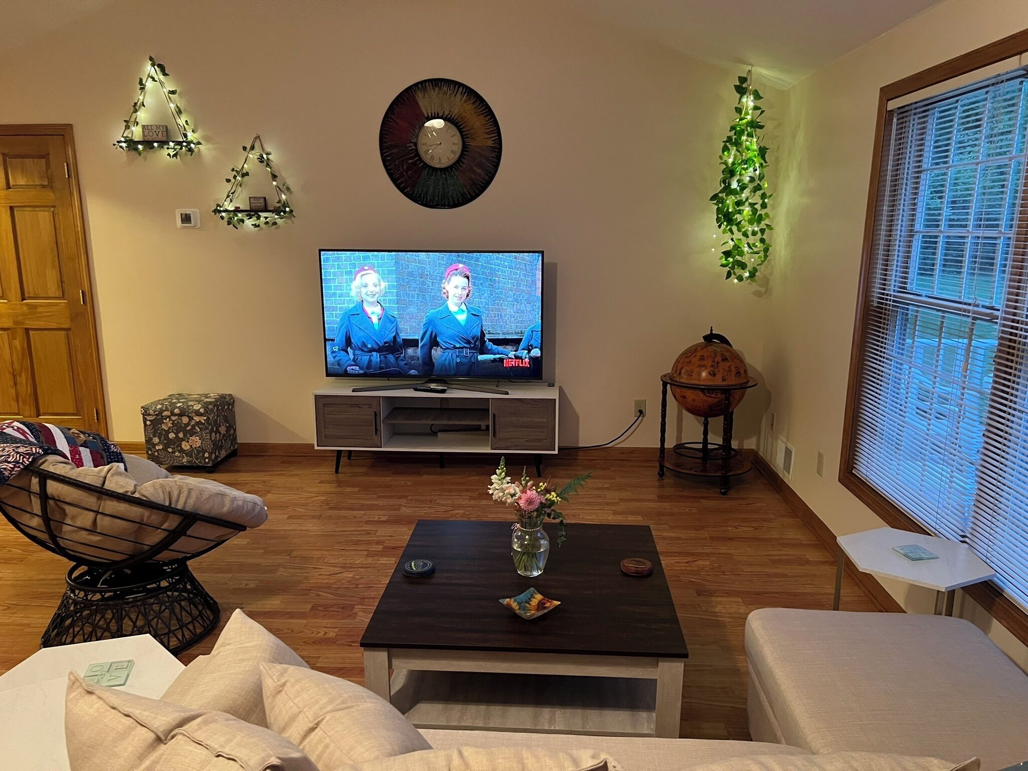 Olohuone, jossa on televisio, puulattia, maljakko, sohvapöytä, sohva ja koristeellinen maapallo.