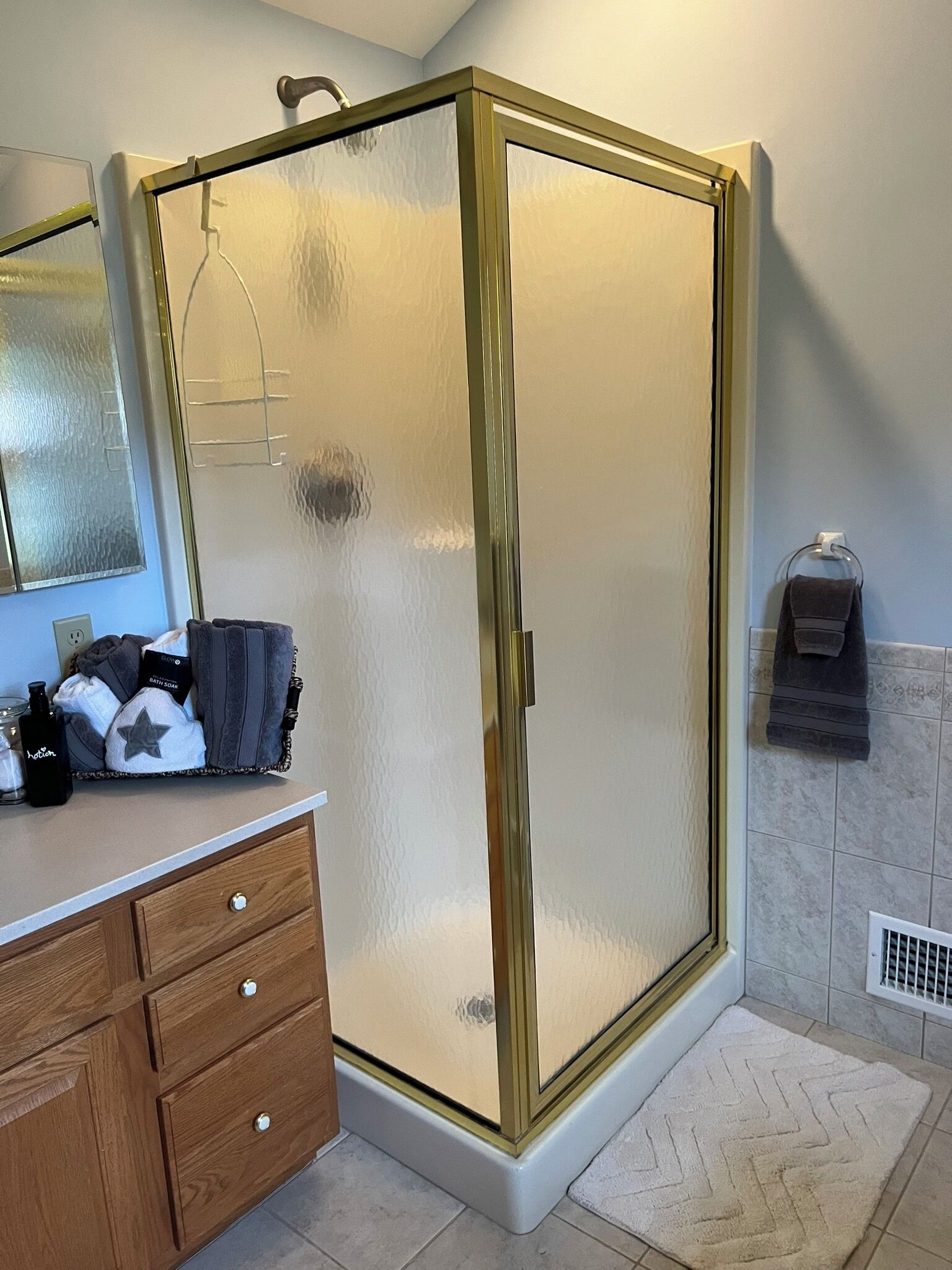 A bathroom with a glass shower enclosure, a wooden vanity with drawers, a towel rack, and a tiled floor.