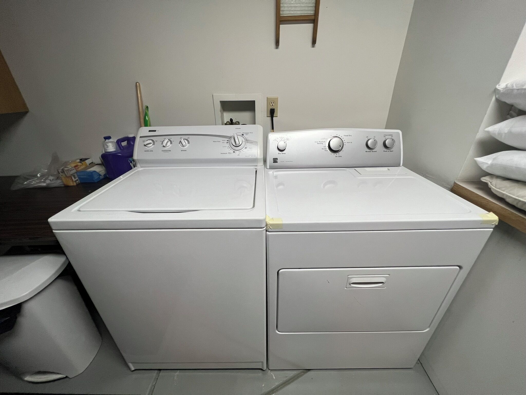 A laundry room with two stacked front-loading washing machines and a small shelf with towels.