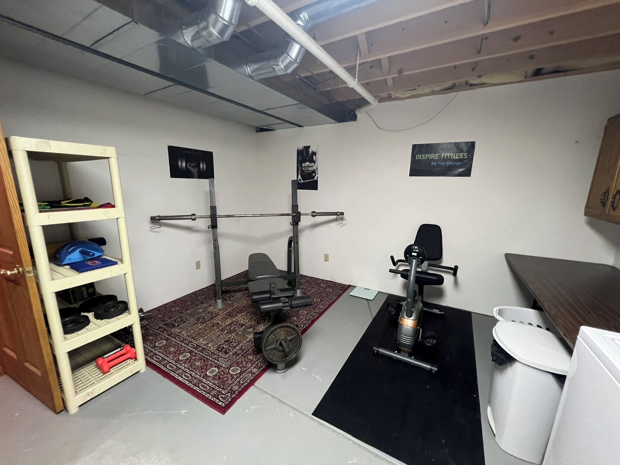 Une salle de sport à domicile équipée d’un support à squat, d’un banc de développé couché et de divers poids.