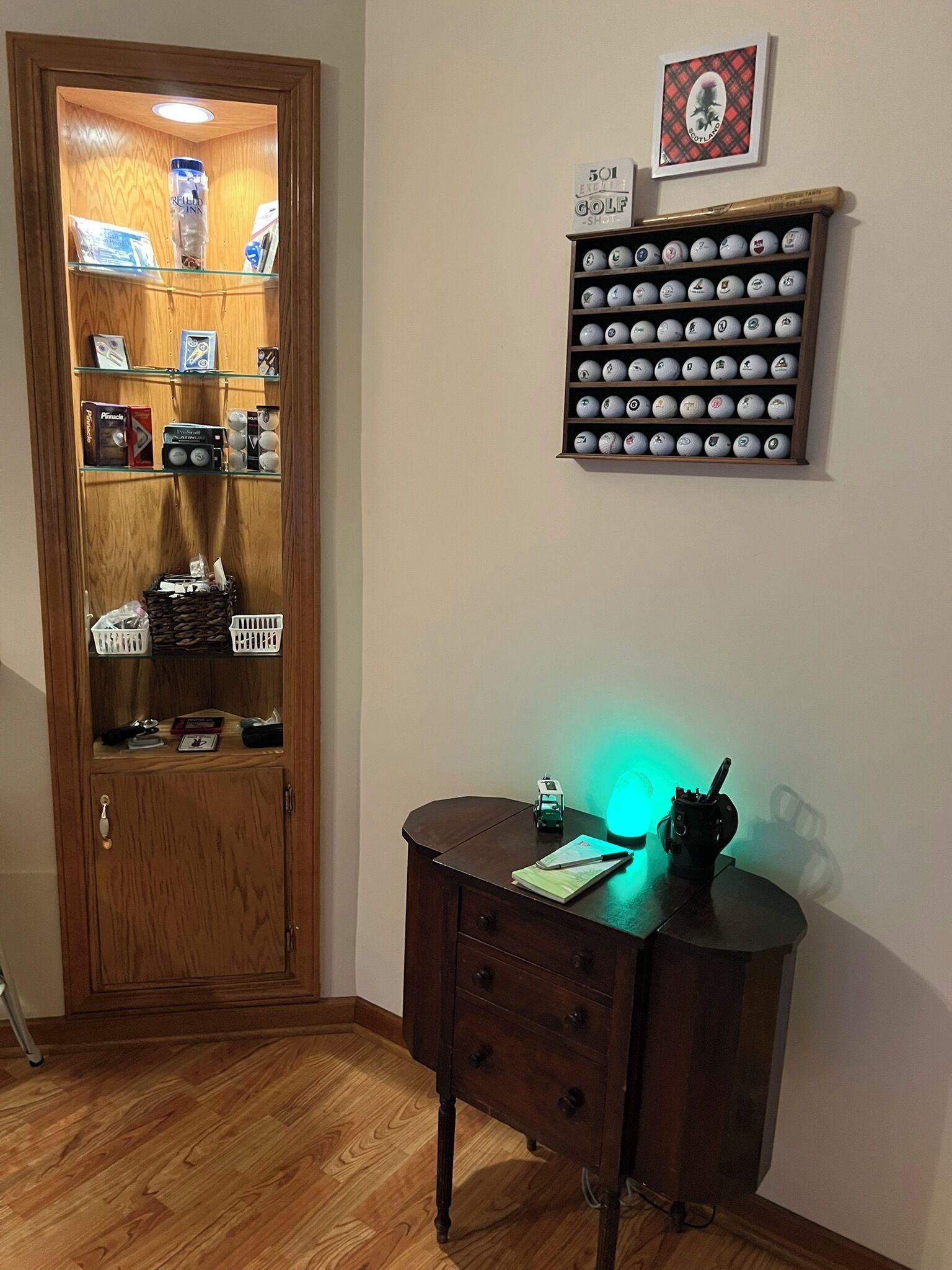 A room with a wooden door leading to a storage area, a desk with a green light, and a wall-mounted golf ball display.