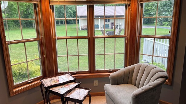Ein Eckzimmer mit Erkerfenster, einem gepolsterten Sessel und einem kleinen Tisch mit dekorativer Ablage.