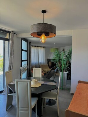 Un comedor con una mesa, sillas, una lámpara colgante y vistas al exterior.