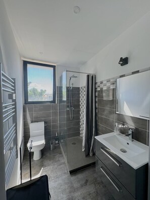 Un baño moderno con cabina de ducha de vidrio, inodoro y tocador con espejo.