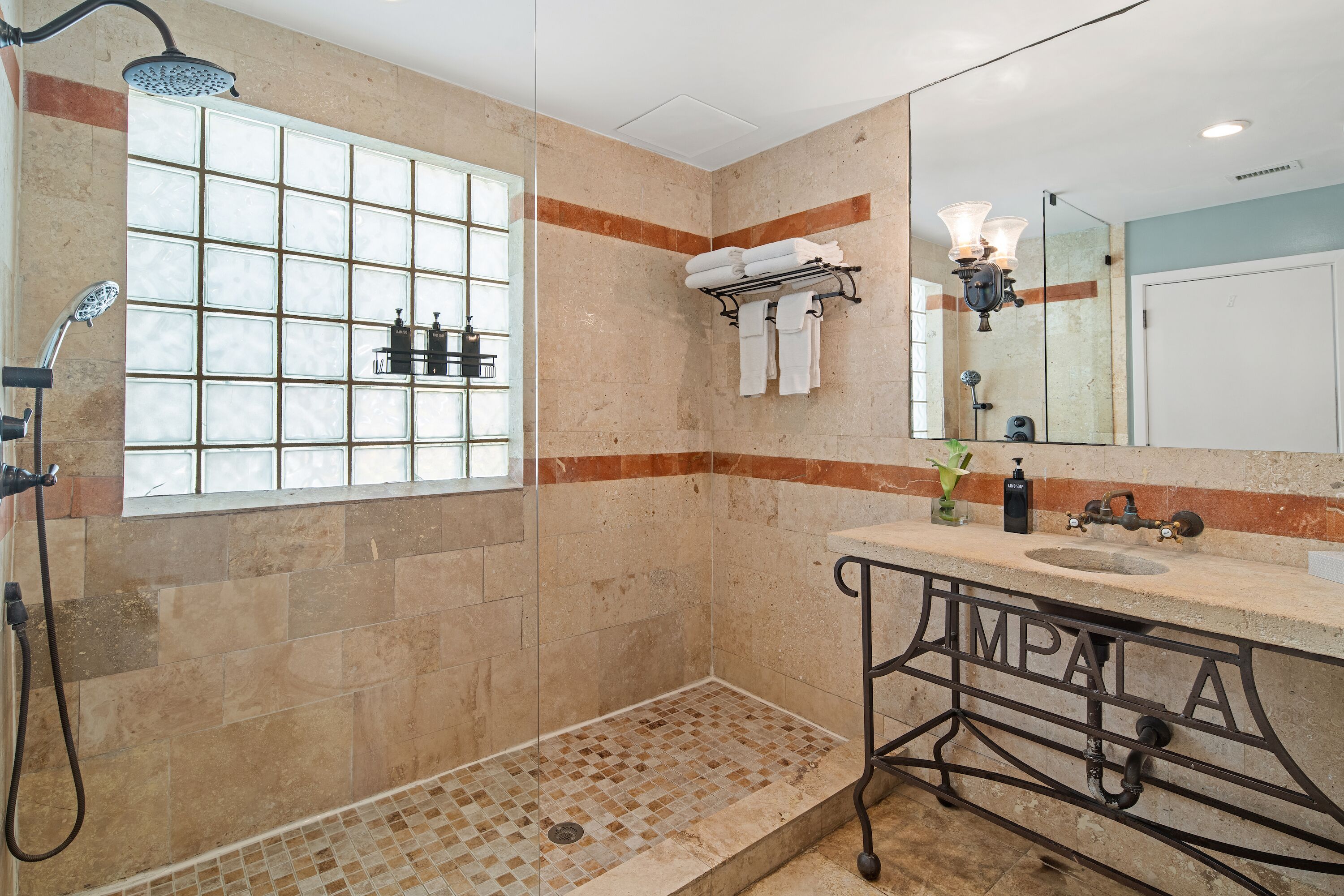 Een badkamer met een douche, wastafel, spiegel en handdoekhouder.