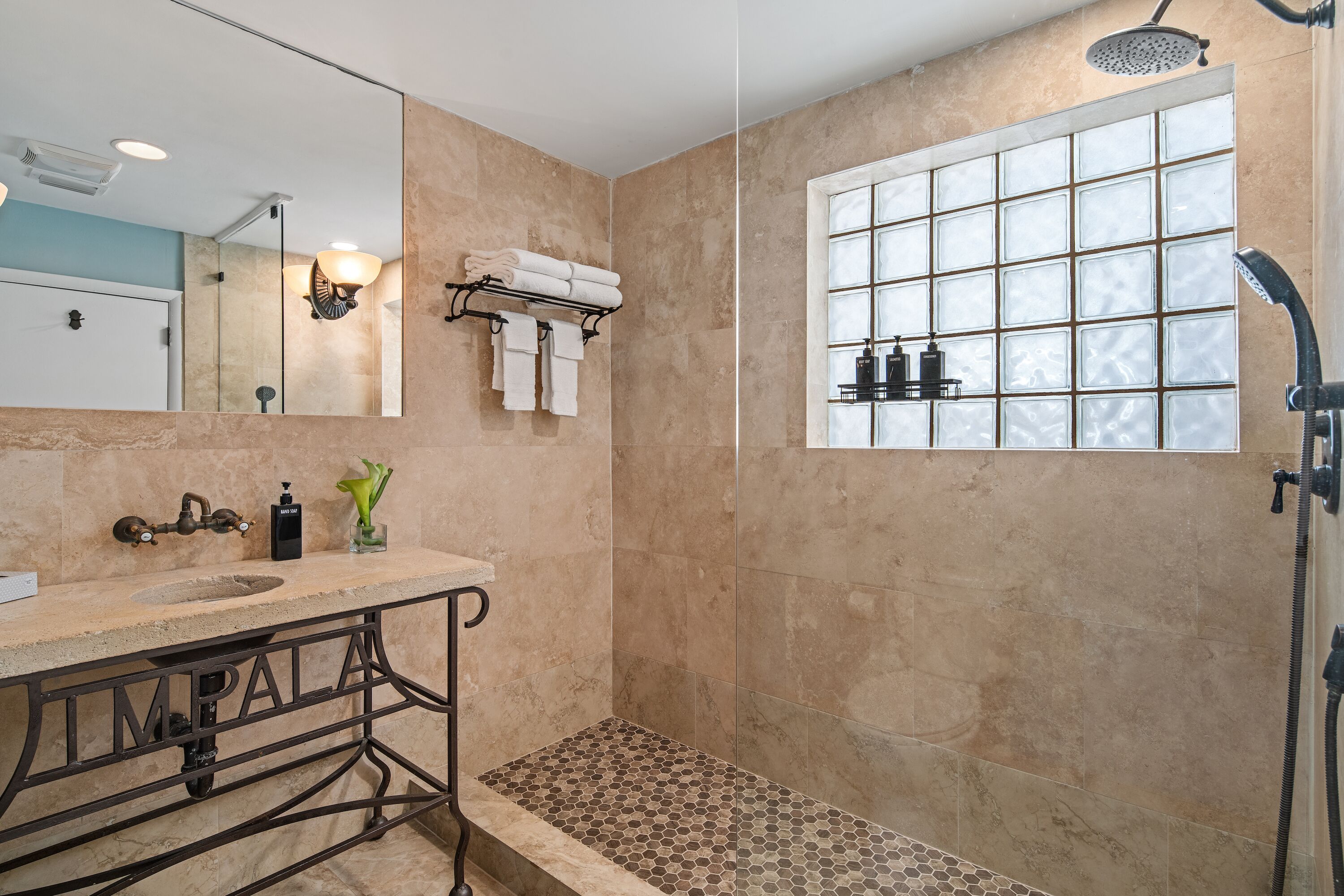 Une salle de bain équipée d’un lavabo, d’un miroir, d’un porte-serviettes, d’une douche et d’une fenêtre à carreaux.