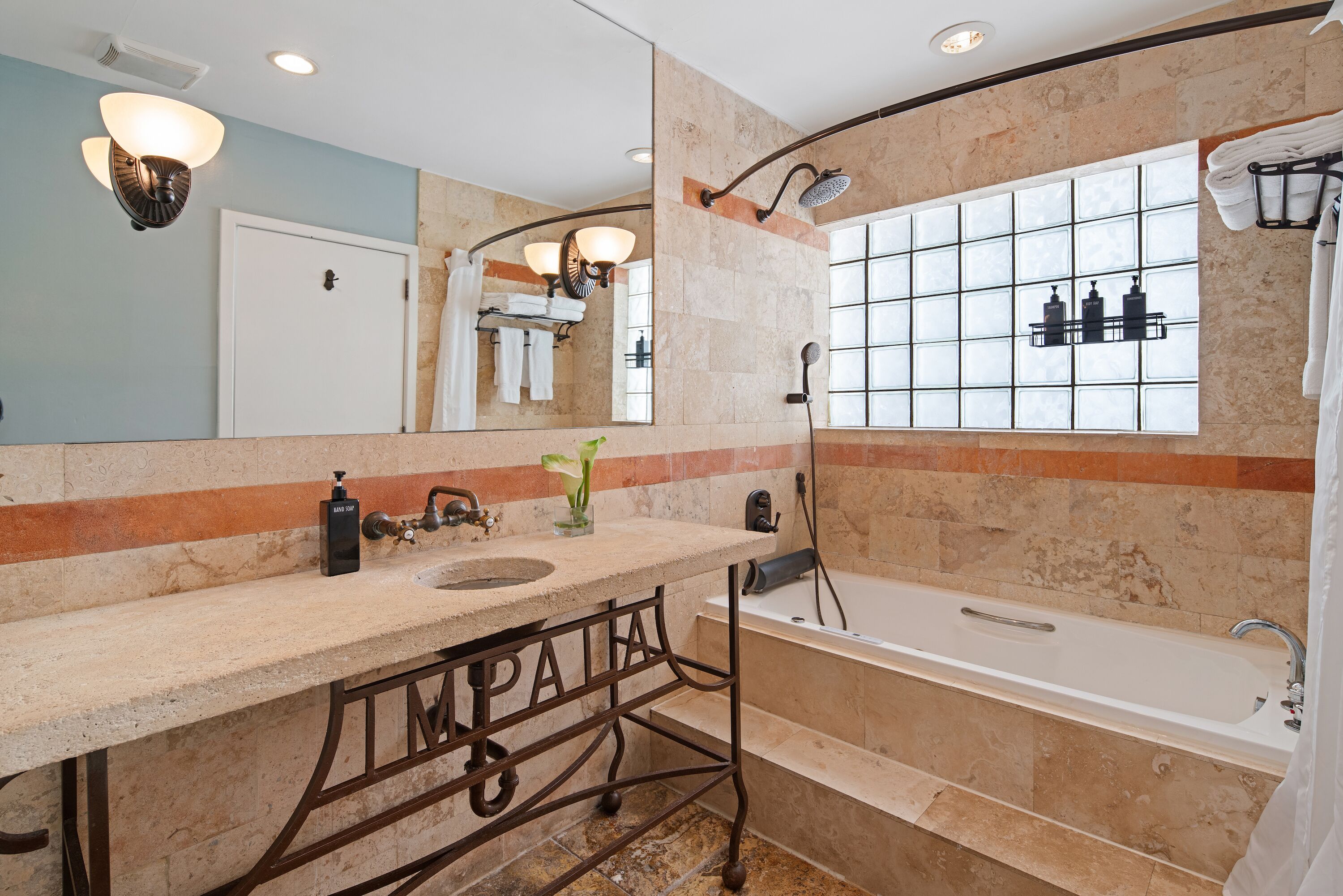 A bathroom with a bathtub, a sink, a mirror, and a window with a view of the outside.