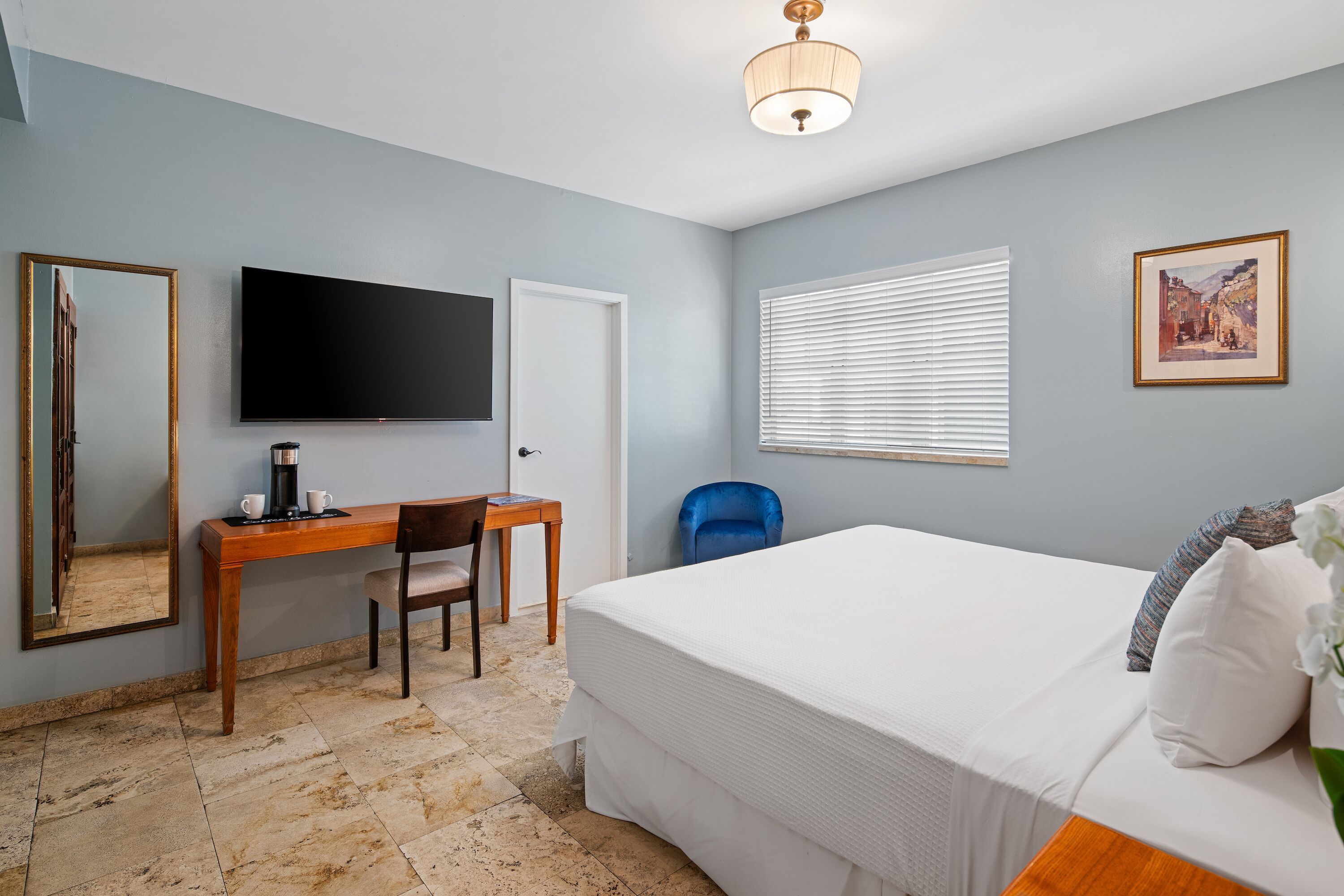 Hotelkamer met een bed, bureau met stoel, televisie, raam met zonwering en een deur.