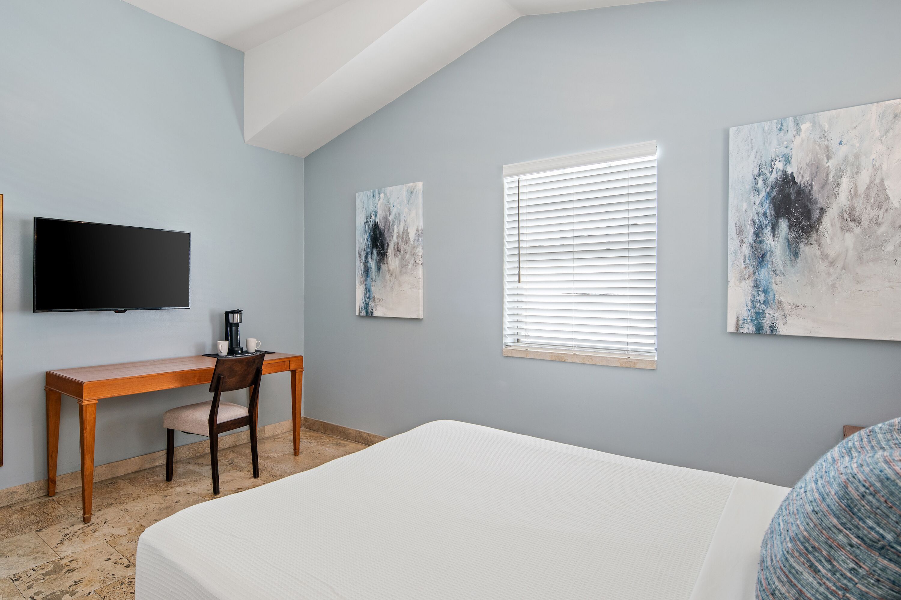Una camera da letto con un letto, una scrivania, una sedia, un televisore e due dipinti astratti alle pareti.