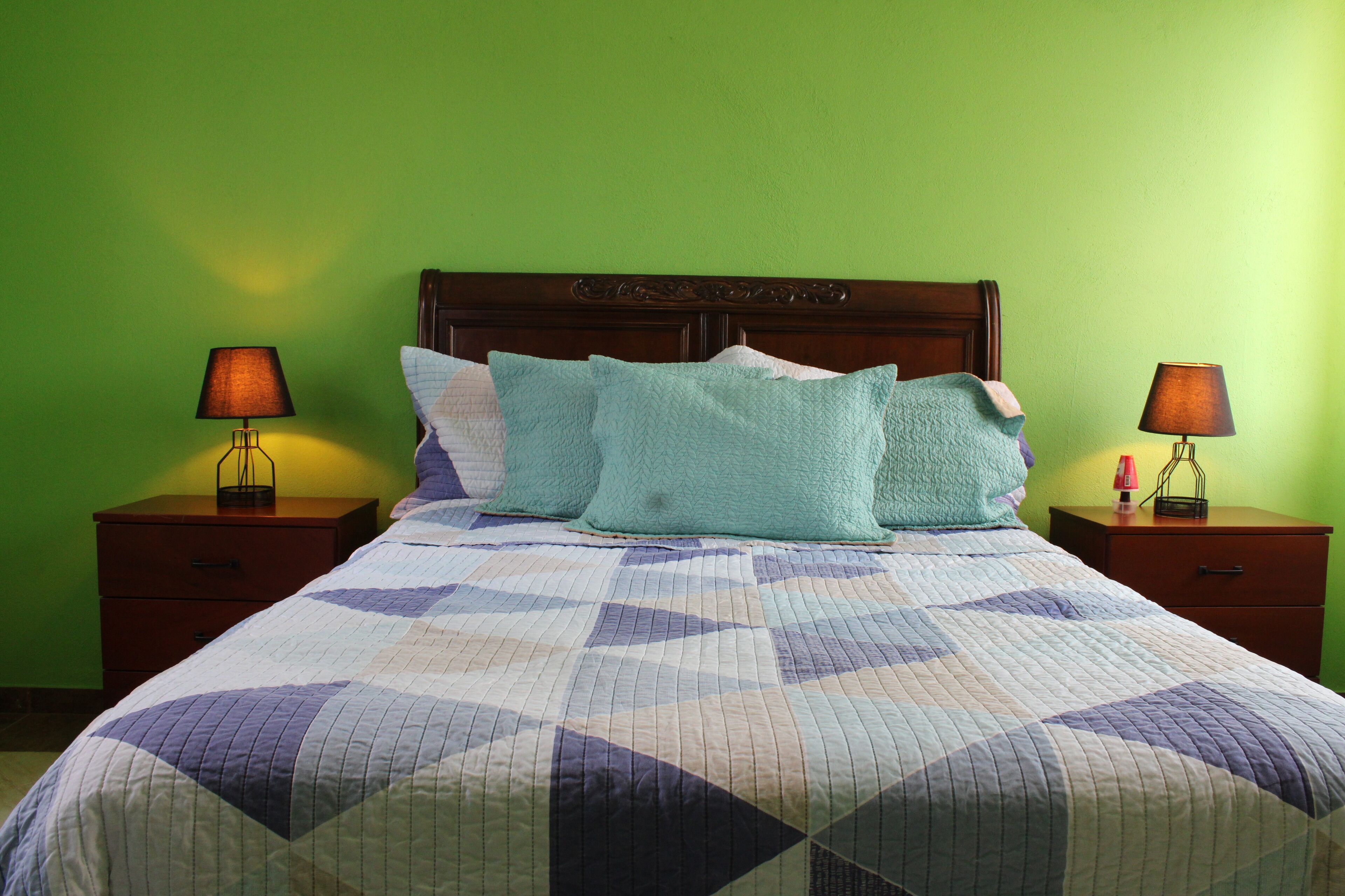 Een bed met een sprei, twee nachtkastjes met lampen, en een groene muur.