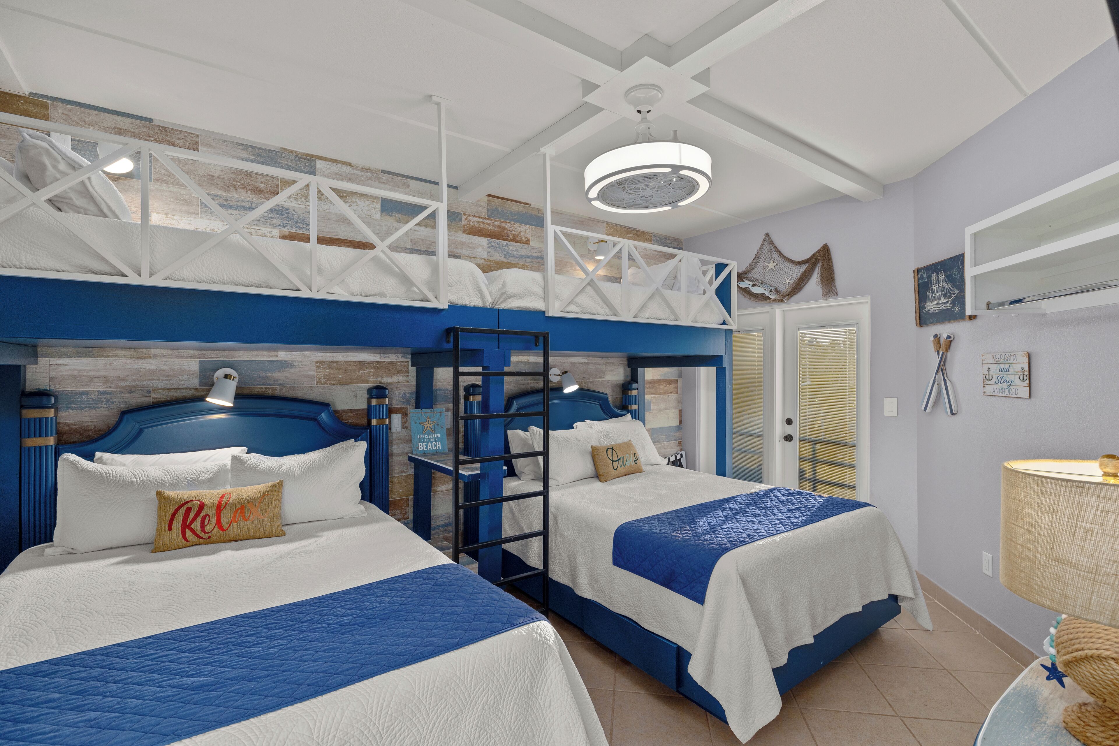 A hotel room with two beds, a loft bed, a ceiling fan, a lamp, and a window with blinds.
