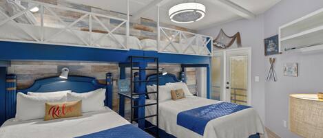 A hotel room with two beds, a loft bed, a ceiling fan, a lamp, and a window with blinds.